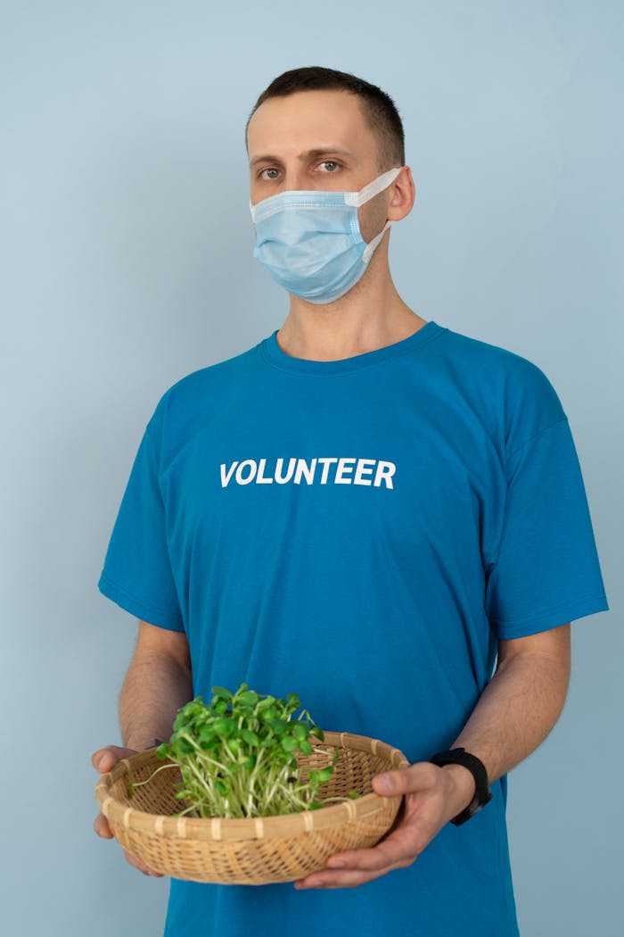 Volunteer wearing mask holds basket of seedlings, promoting eco-friendly initiatives.